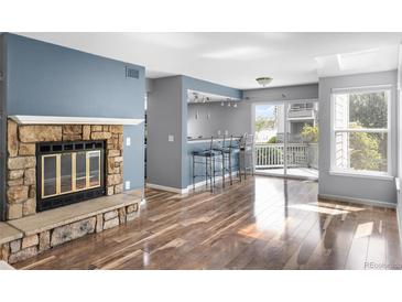 Open living room featuring hardwood floors, a stone fireplace, and access to the outdoor deck at 6861 Xavier Cir # 3, Westminster, CO 80030