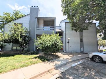 Attractive two-story condo with gray siding, chimney, manicured lawn, and lush trees at 14006 E Stanford Cir # K08, Aurora, CO 80015
