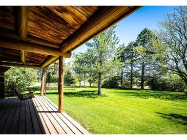 Covered porch with wooden flooring and a swing overlooks the expansive lawn and trees at 2965 Wagner St, Strasburg, CO 80136