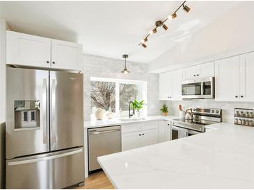 Bright kitchen features stainless steel appliances, white cabinets, marble backsplash, and quartz countertops at 12050 Dahlia Dr, Thornton, CO 80241