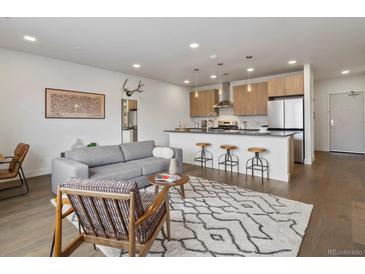 Open-concept living room and kitchen with modern finishes and hardwood flooring at 1898 S Bannock St # 209, Denver, CO 80223
