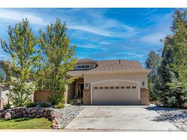 Charming beige home with a two-car garage, stone accents, and a well-manicured front yard under a bright blue sky at 740 Deer Clover Cir, Castle Pines, CO 80108