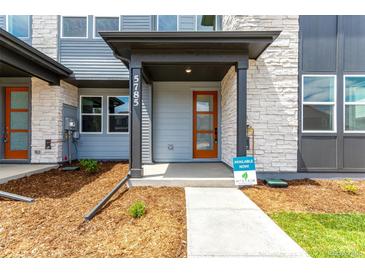 Inviting covered front entryway featuring a modern wood door, stone accents, and landscaped mulch beds at 5785 N Jericho Way, Aurora, CO 80019