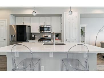 Modern kitchen features white cabinets, stainless steel appliances, and a large center island with seating at 9612 Reunion Pkwy, Commerce City, CO 80022