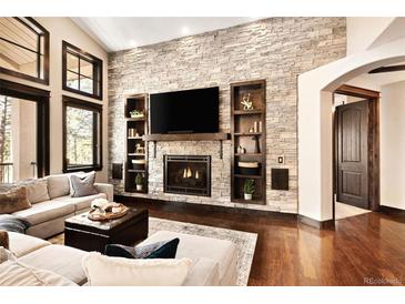 Cozy living room with stone fireplace, built-in shelving, and hardwood floors at 8294 Wild Timber Dr, Franktown, CO 80116