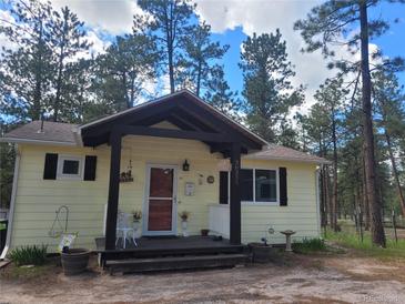 Charming cottage-style home with a welcoming front porch and beautifully maintained landscaping surrounded by mature trees at 36351 County Road 21, Elizabeth, CO 80107
