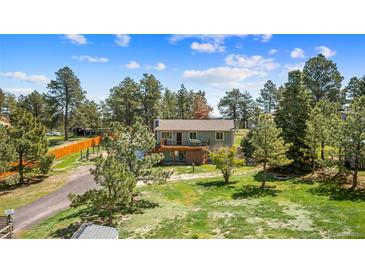 Charming two-story home with a deck, set amongst lush trees, and a green lawn at 1151 Buttercup Rd, Elizabeth, CO 80107