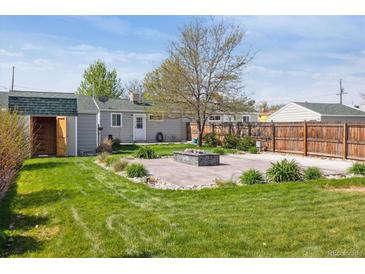 Landscaped backyard featuring a stone patio with built-in fire pit, green grass and partial fence at 6245 W 53Rd Ave, Arvada, CO 80002