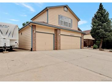 Tan two-story home featuring a spacious driveway and a two-car garage with brick accents at 2957 W Rowland Ave, Littleton, CO 80120