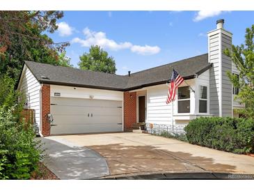 Charming home featuring a two-car garage, red brick, concrete driveway, an American flag, and mature landscaping at 1102 Conifer Ct, Highlands Ranch, CO 80126