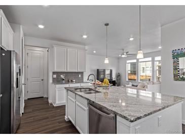 Open kitchen area with a granite island and stainless appliances leads into the living room with dark hardwood floors at 723 176Th Ave, Broomfield, CO 80023