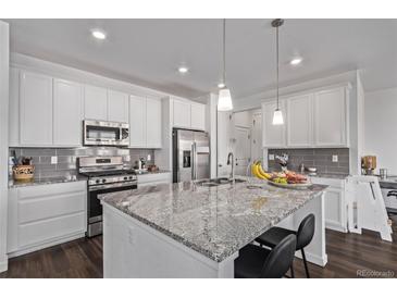 Bright kitchen features white cabinets, stainless steel appliances, a large island with a stone countertop, and modern pendant lighting at 723 176Th Ave, Broomfield, CO 80023