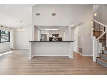 Open-concept living room view to kitchen with bar, and staircase with wood-look flooring and neutral walls at 540 S Forest St # 3-204, Denver, CO 80246
