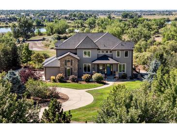 Elegant two-story home with lush landscaping, featuring a stone facade and a circular driveway at 12648 Waterside Ln, Longmont, CO 80504