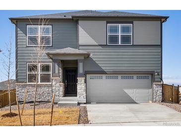 A modern, two-story home with gray siding, a stone facade, and a two-car garage on a sunny day at 8879 Sedalia St, Commerce City, CO 80022