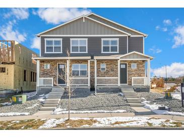 Traditional-style home featuring stone accents, gray siding, and a charming front porch with white railing at 18714 E 99Th Ave, Commerce City, CO 80022