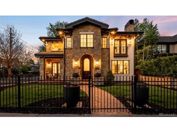 Stunning stone home with manicured lawn, fence, and illuminated arched entryway at 2400 S Columbine St, Denver, CO 80210