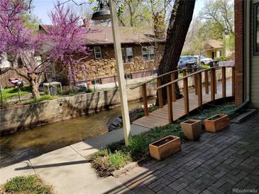 Charming backyard with patio, bridge over creek, and views of mature landscaping and exterior of stone house at 1633 18Th St # 2, Boulder, CO 80302
