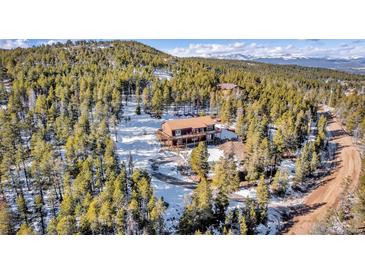 Aerial view of a cozy cabin surrounded by pine trees and a snowy landscape at 255 Divide View Dr, Golden, CO 80403