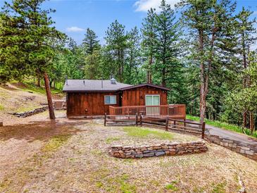 Charming single-story home with a wooden deck and beautiful landscaping surrounded by lush greenery and tall trees at 23778 Inca Rd, Indian Hills, CO 80454