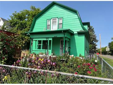 Charming two-story home with a bright green exterior and flourishing flower garden in front at 4047 Lowell Blvd, Denver, CO 80211