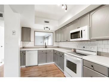 Updated kitchen boasts grey cabinetry, subway tile backsplash, white appliances, and wood-look flooring at 1279 S Sable Blvd, Aurora, CO 80012