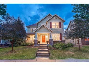 Inviting two-story home with a manicured lawn, orange front door, and charming architectural details at 13053 Umatilla Ct, Denver, CO 80234