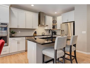 Modern kitchen features white cabinets, stainless steel appliances, and a black countertop island with seating at 24686 E Florida Ave, Aurora, CO 80018