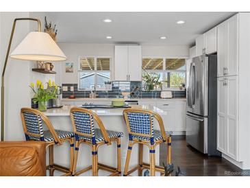 Bright kitchen with breakfast bar, white cabinetry, stainless appliances, and stylish decor at 3011 Oneida St, Denver, CO 80207