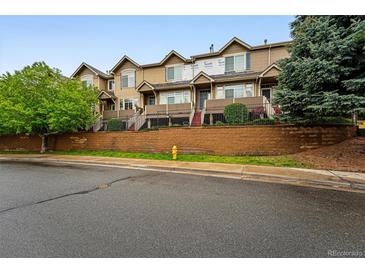 Townhome-style condominiums with brown siding and a brick retaining wall at street level with trees on either side at 5555 E Briarwood Ave # 2604, Centennial, CO 80122