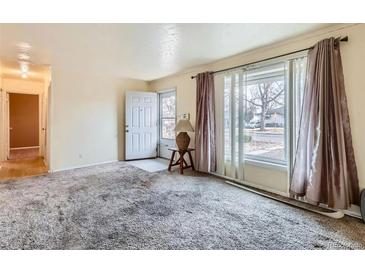 A bright living room featuring plush carpet, a large window with curtains, and a view of the front yard at 1931 Dayton St, Aurora, CO 80010