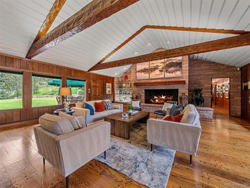 Spacious living room features a brick fireplace, wood floors, wood paneled walls, and beamed vaulted ceiling at 32453 Upper Bear Creek Rd, Evergreen, CO 80439