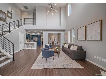 Open-concept living room features high ceilings, modern chandelier, wood floors, and seamless flow to kitchen and dining area at 10523 Ashfield St # 5C, Highlands Ranch, CO 80126