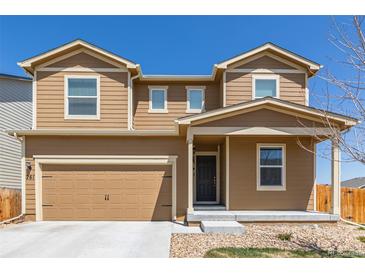 Tan two-story home with a two car garage and covered front porch on a clear day at 261 Mesa Ave, Lochbuie, CO 80603