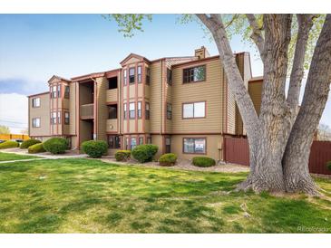 Three-story tan apartment building with red trim surrounded by bushes and green lawn at 8770 Corona St # 101, Denver, CO 80229