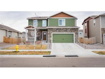 Charming two-story home features a green exterior, stone accents, and a matching green two-car garage at 676 Hearthstone Ave, Brighton, CO 80601