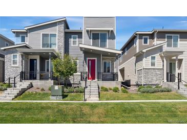 Modern townhome featuring gray siding, stone accents, a red front door, and well-maintained landscaping at 12314 Hayloft Ln, Thornton, CO 80241
