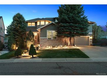 Inviting two-story home with stone accents, lush landscaping, and illuminated front yard at twilight at 8406 Winter Berry Dr, Castle Pines, CO 80108