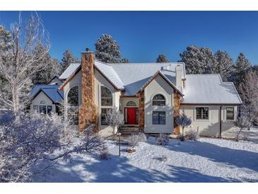Stunning home with stone chimney, snow-covered roof, and bright red door in a picturesque winter setting at 2880 Lake Meadow Dr, Monument, CO 80132