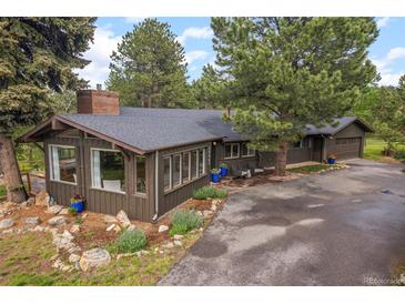 Charming home with a sunroom, a paved driveway, and beautifully landscaped with flower pots and rock features at 29663 Paint Brush Dr, Evergreen, CO 80439