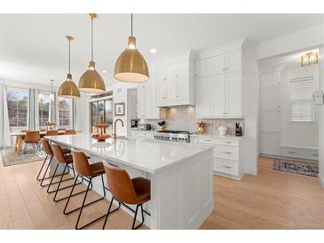 Bright kitchen features white cabinets, island with seating, gold hardware and lighting, and stainless appliances at 15 Latigo Pl, Littleton, CO 80123