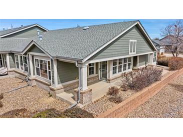 A green shingled home exterior with brick foundation, a small patio, and beige trim under a bright blue sky at 15123 Xenia St, Thornton, CO 80602