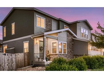 Charming home featuring stone accents, a welcoming front porch, and manicured landscaping under a colorful dusk sky at 6894 E 133Rd Pl, Thornton, CO 80602