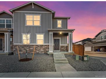Two-story home boasts stone accents, neutral gray siding, and a welcoming front porch, set against a colorful twilight sky at 259 E 4Th St, Berthoud, CO 80513