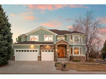 Two-story home featuring a three car garage, green stucco, and stone features at dusk at 1942 Kentmere Dr, Longmont, CO 80504