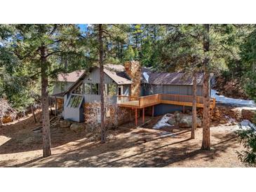 Charming gray home with a stone chimney and a wooden deck nestled amongst tall pine trees at 4835 Abo Ln, Monument, CO 80132