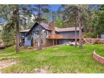 Charming multi-level home featuring a stone chimney and inviting wooden deck surrounded by lush greenery and mature trees at 4835 Abo Ln, Monument, CO 80132