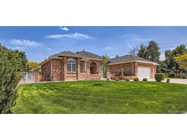 Charming brick home featuring lush lawn, attached garage, manicured landscaping, and mature trees on a sunny day at 3810 Urban St, Wheat Ridge, CO 80033