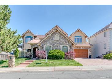 Charming stone-accented home featuring a tile roof, manicured lawn and mature trees at 16713 W Archer Ave, Golden, CO 80401