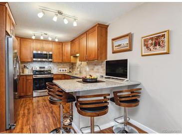 Well-lit kitchen features wood cabinets, stainless steel appliances, granite countertops, and breakfast bar with three chairs at 9320 E Center Ave # 7A, Denver, CO 80247